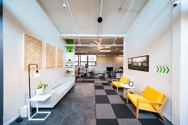 Lounge area with sofas, yellow accent chair, and open desks under skylights at Platform Coworking